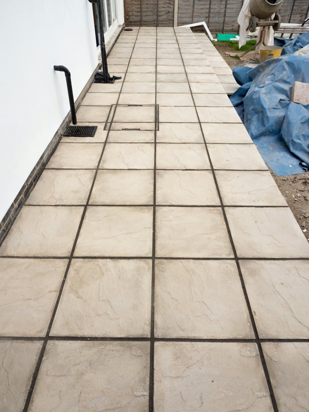 Neben einer weißen Hauswand liegen frisch verlegte, beige Terrassenplatten.