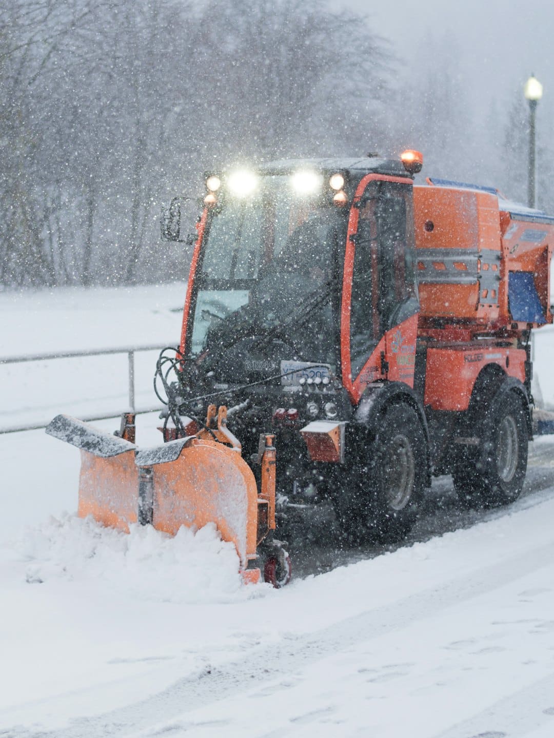 Ein orangefarbener Schneepflug räumt während eines Sturms eine Straße frei.