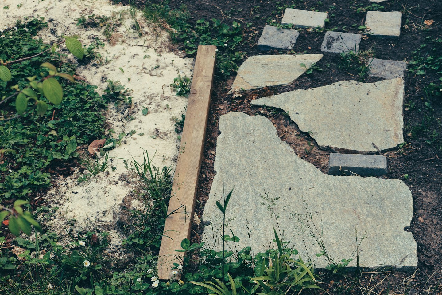 Unregelmäßige Steinplatten werden für einen Gartenweg auf Erde verlegt.