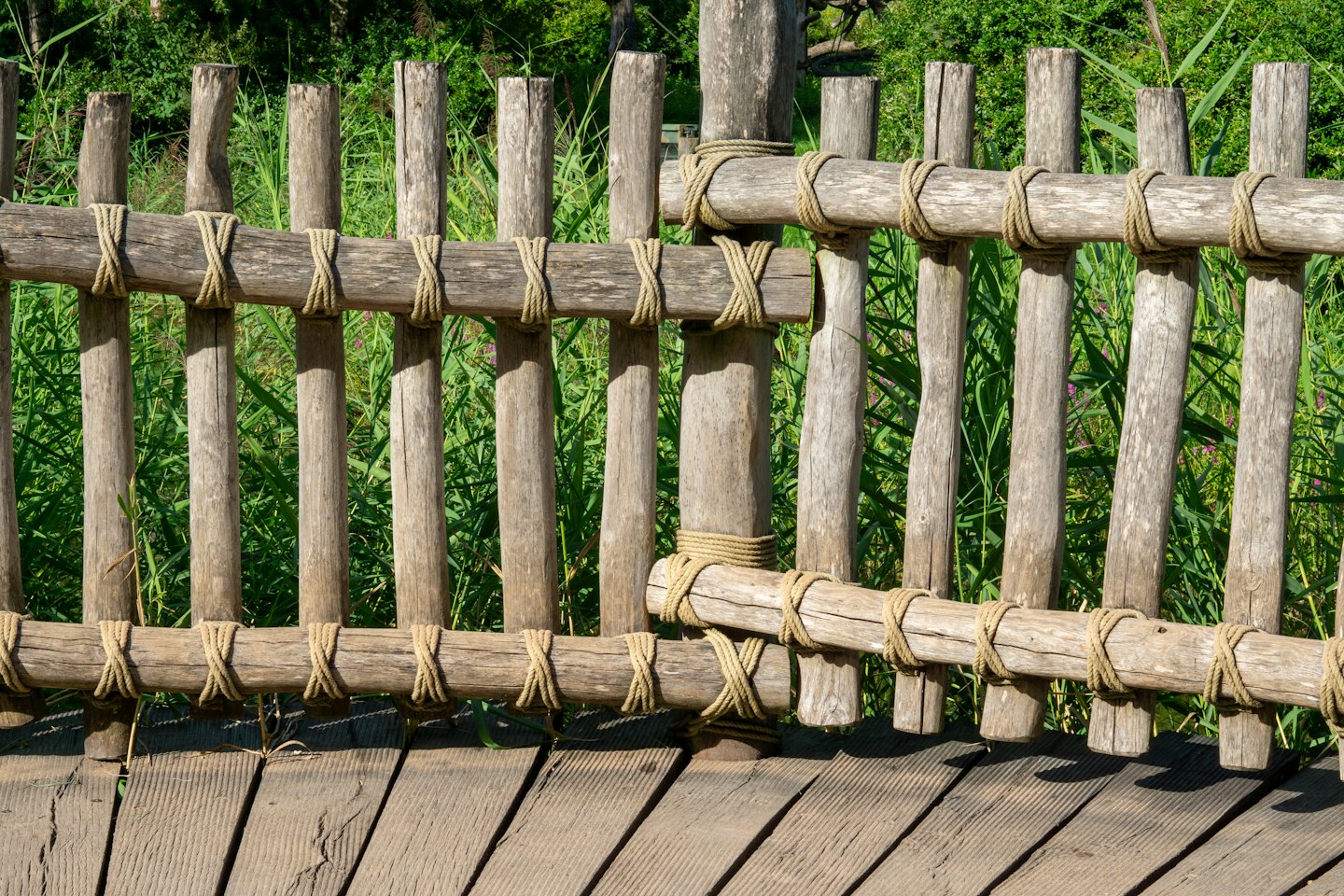 Verwitterter Holzzaun, der mit einem Seil an einer Promenade befestigt ist.
