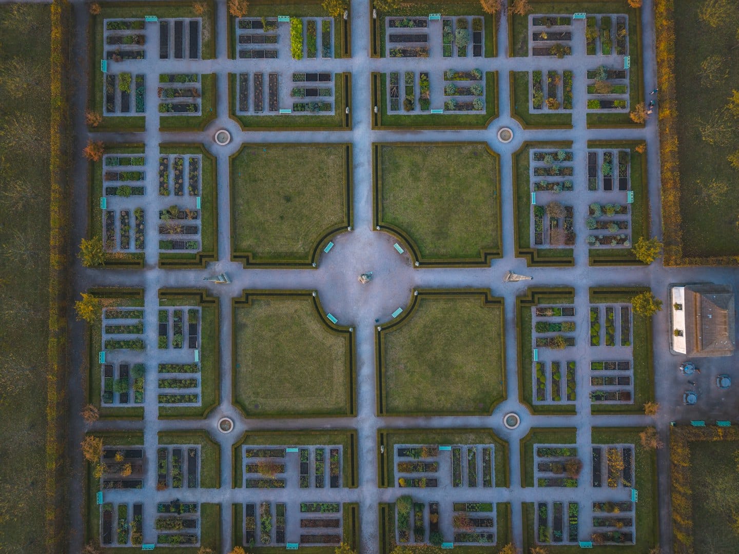 Symmetrischer formaler Garten mit geschnittenen Hecken und grauen Steinwegen.