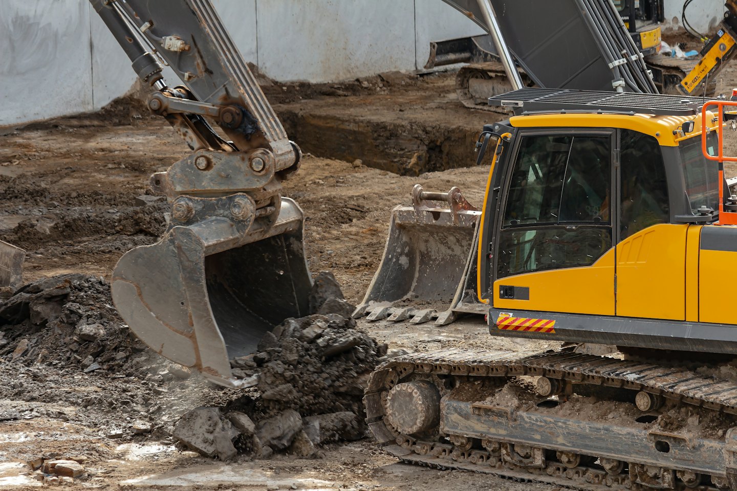 Gelber Baggerarm gräbt braune Erde auf einer Baustelle.